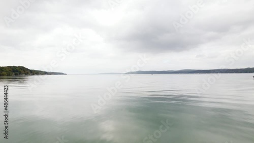 Fast drone shot flying over Crystal Lake in Beulah Michigan during early autumn on a gloomy day with hills and trees in the background, with grey clouds and a moody setting. photo