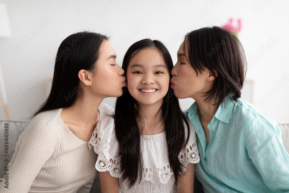 Happy little Asian girl being kissed by her mother and grandmother at home Happy little Asian girl being kissed by her mother and grandmother at home