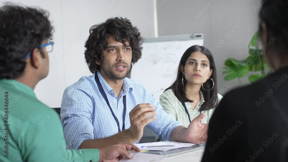 Young Indian man coach sitting holding meeting with diverse work team discussing sharing ideas in conference room, multi ethnic people or colleague brainstorm talking cooperating at office. Young Indian man coach sitting holding meeting with diverse work team discussing sharing ideas in conference room, multi ethnic people or colleague brainstorm talking cooperating at office.