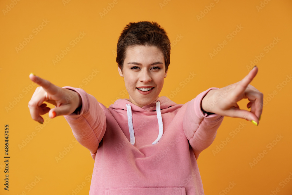 Happy cheerful girl pointing finger at camera over yellow background Happy cheerful girl pointing finger at camera over yellow background