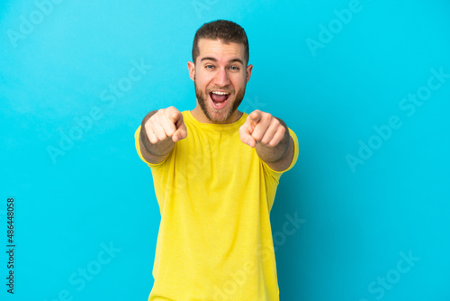 Young handsome caucasian man isolated on blue background surprised and pointing front