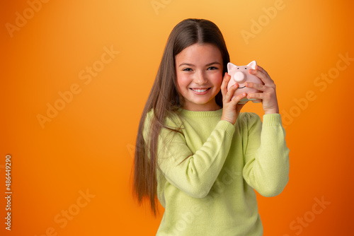 Teen girl with piggy bank on orange color background.