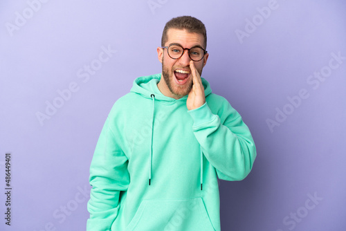 Young handsome caucasian man isolated on purple background shouting with mouth wide open © luismolinero