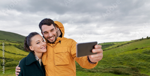 technology, travel and tourism concept - happy couple taling selfie with smartphone over farmland fields and hills at wild atlantic way in ireland © Syda Productions