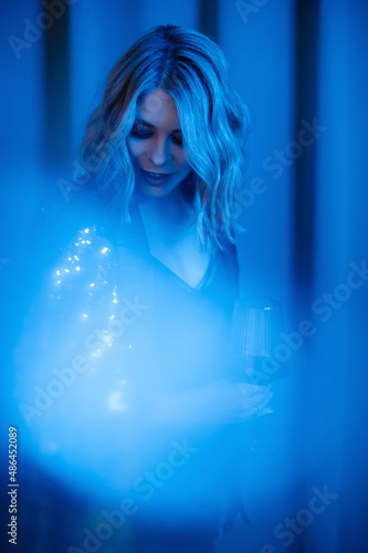 Charming model with glass of wine posing in neon blue light