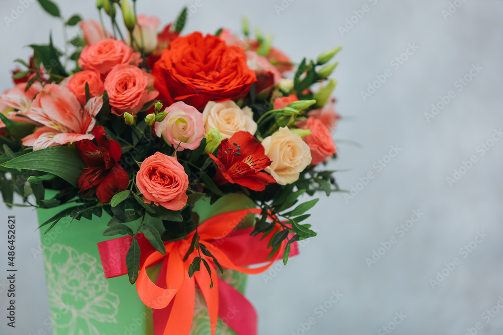 Red bouquet of rose, alstroemeria and eustoma in a green paper gift box on a gray background.