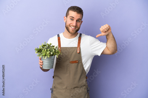 Gardener caucasian man holding a plant isolated on yellow background proud and self-satisfied