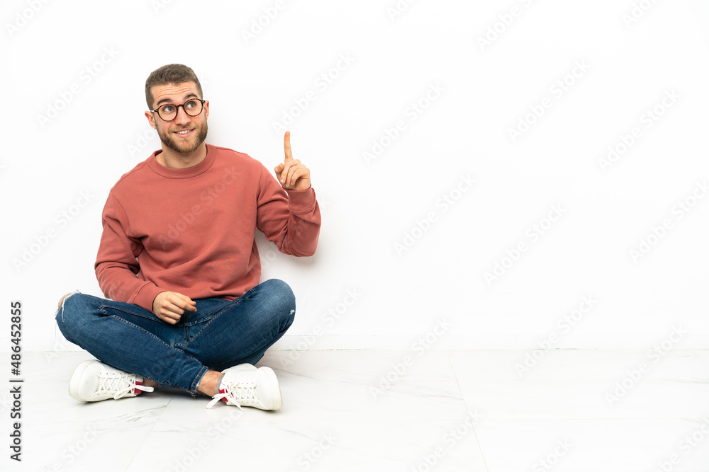 Young handsome man sitting on the floor pointing up and surprised