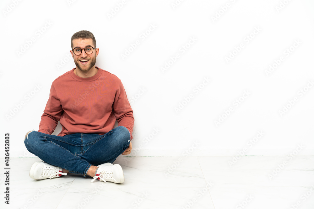 Young handsome man sitting on the floor with surprise facial expression Young handsome man sitting on the floor with surprise facial expression