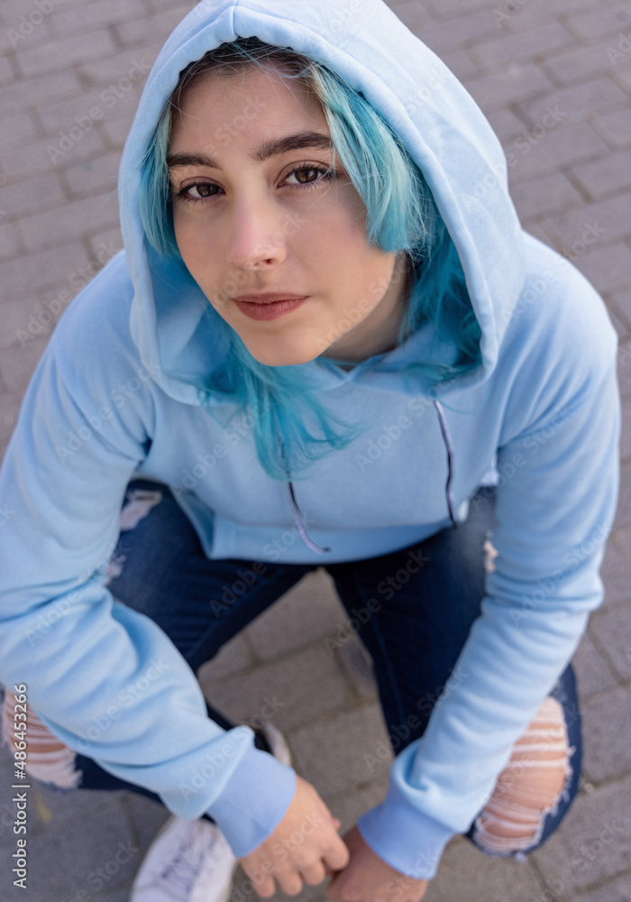 Blue haired Teenage girl in light blue oversize hoodie sitting on her haunches Blue haired Teenage girl in light blue oversize hoodie sitting on her haunches