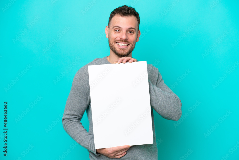 Young Brazilian man holding an empty placard isolated on blue background holding an empty placard with happy expression Young Brazilian man holding an empty placard isolated on blue background holding an empty placard with happy expression
