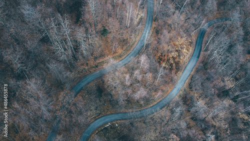 Aerial high angle view of narrow winding curvy mountain road among the trees in winter forest. Bird's eye view landscape.