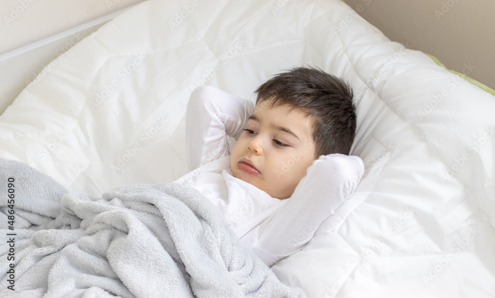 cute little kid is laying on bed with both hands under the head and crooking his lips. bedtime in the afternoon. relax and rest concept. white t shirt and white blanket. 4 years old caucasian hansome cute little kid is laying on bed with both hands under the head and crooking his lips. bedtime in the afternoon. relax and rest concept. white t shirt and white blanket. 4 years old caucasian hansome