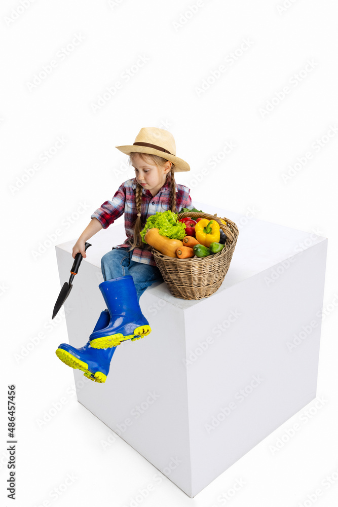 One cute little girl, emotive kid in image of farmer, gardener with large basket of vegetables isolated on white background. Concept of job, work, childhood, games