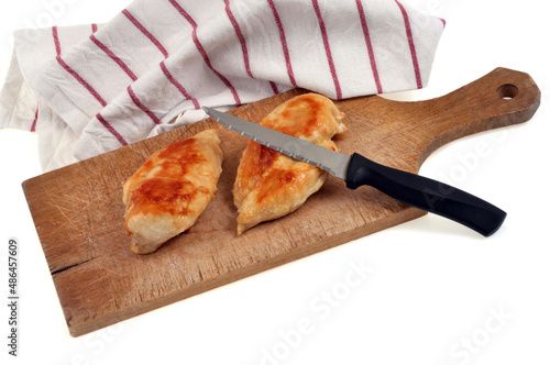 Blancs de poulet cuits sur une planche à découper avec un couteau à côté d'un torchon sur fond blanc