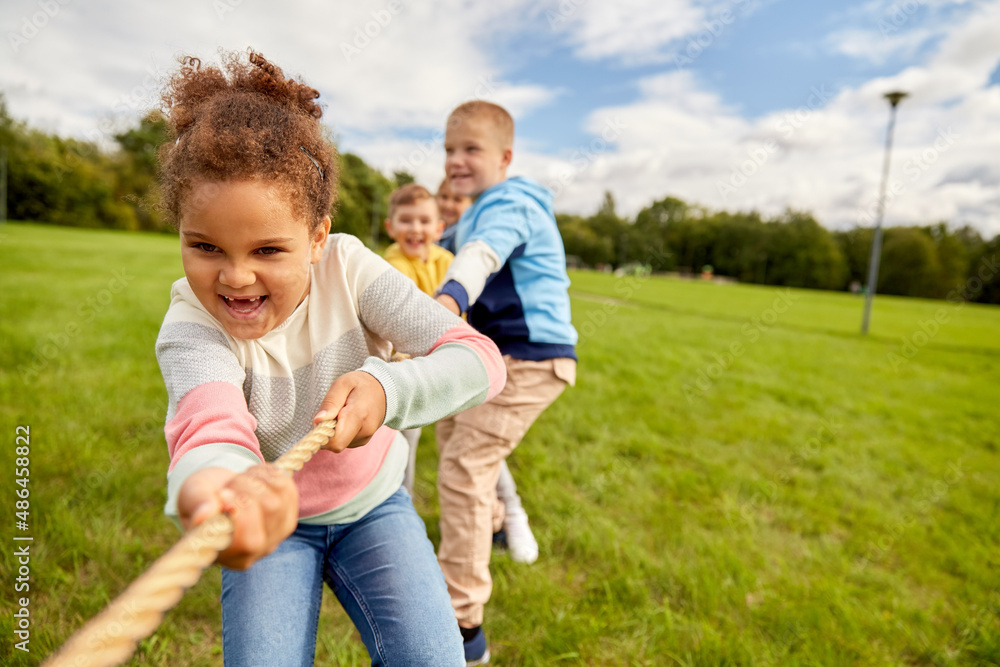 childhood, leisure and people concept - group of happy kids playing tug-of-war game and running at park