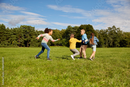 childhood, leisure and people concept - group of happy kids playing tag game and running at park