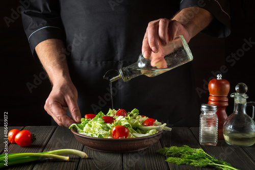 Professional chef pours oil into a salad bowl in the kitchen. Cooking delicious and healthy food with a set of vitamins