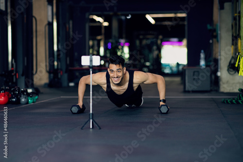Athletic Arab Man Making Dumbbell Push-Ups While Recording Content On Smartphone Camera
