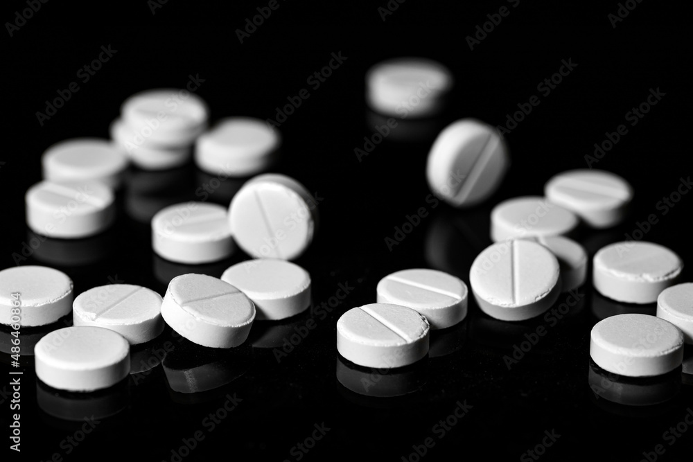 Close up of white painkiller tablet on a reflective black background Close up of white painkiller tablet on a reflective black background