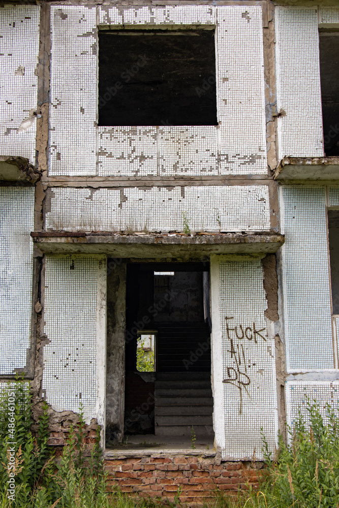 A damaged entrance at a abandoned panel house with decorative facade of small white tiles. A damaged entrance at a abandoned panel house with decorative facade of small white tiles.