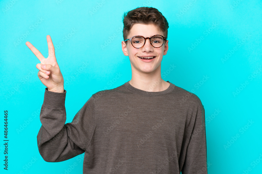 Teenager Russian man isolated on blue background smiling and showing victory sign Teenager Russian man isolated on blue background smiling and showing victory sign