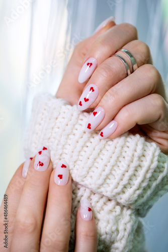 Women's winter manicure with hearts for Valentine's Day. Well-groomed female hand with beautiful nails. Decorative gel polish in the salon. 