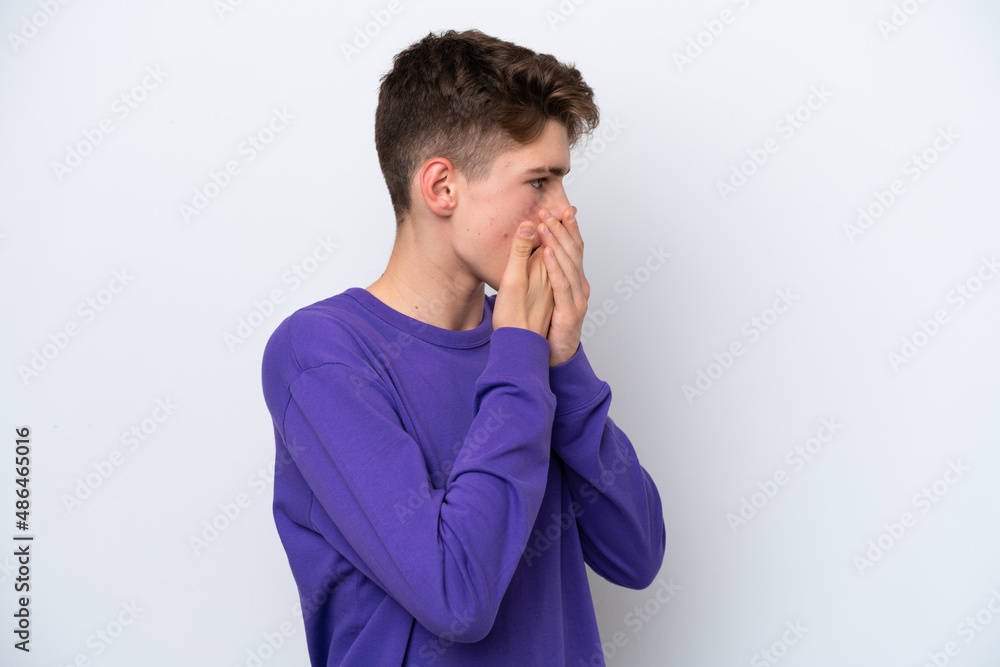 Teenager Russian man isolated on white background covering mouth and looking to the side Teenager Russian man isolated on white background covering mouth and looking to the side