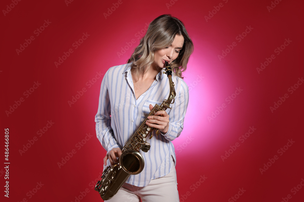 Fototapeta premium Beautiful young woman playing saxophone on red background