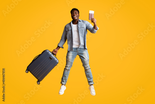 Canvas Print Emotional african american guy with suitcase and flight tickets jumping