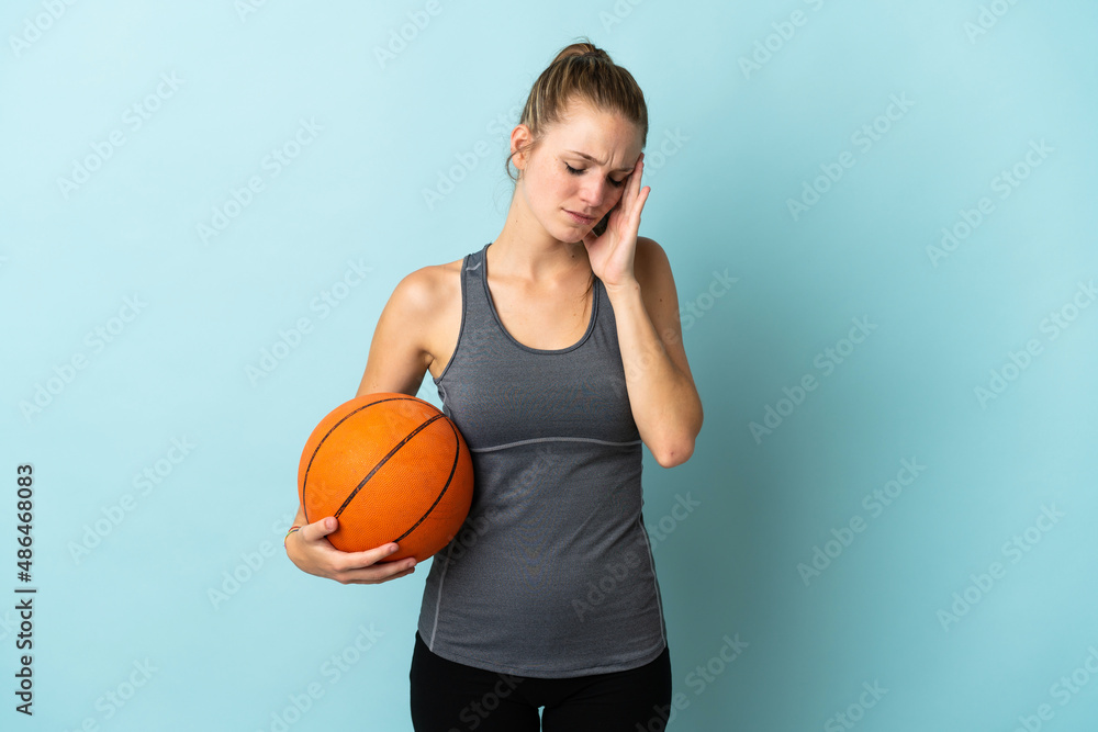 Young woman playing basketball isolated on blue background with headache