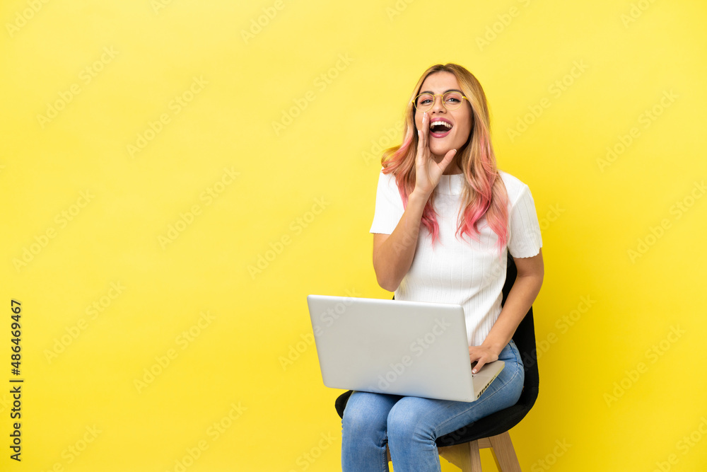 Naklejka premium Young woman sitting on a chair with laptop over isolated yellow background shouting with mouth wide open