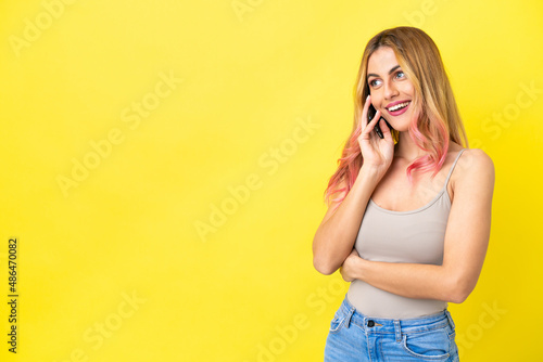 Young woman over isolated yellow background keeping a conversation with the mobile phone © luismolinero