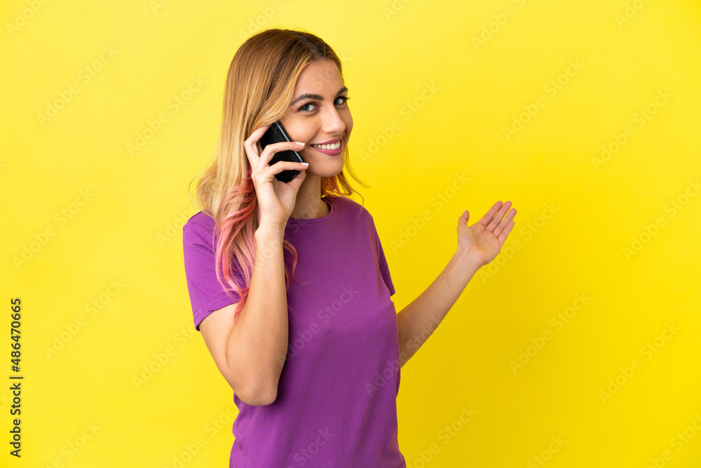 Young woman using mobile phone over isolated yellow background extending hands to the side for inviting to come Young woman using mobile phone over isolated yellow background extending hands to the side for inviting to come