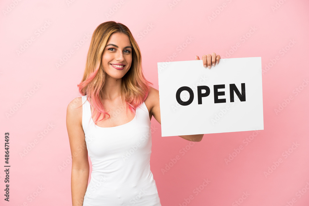 Young woman over isolated pink background holding a placard with text OPEN with happy expression Young woman over isolated pink background holding a placard with text OPEN with happy expression