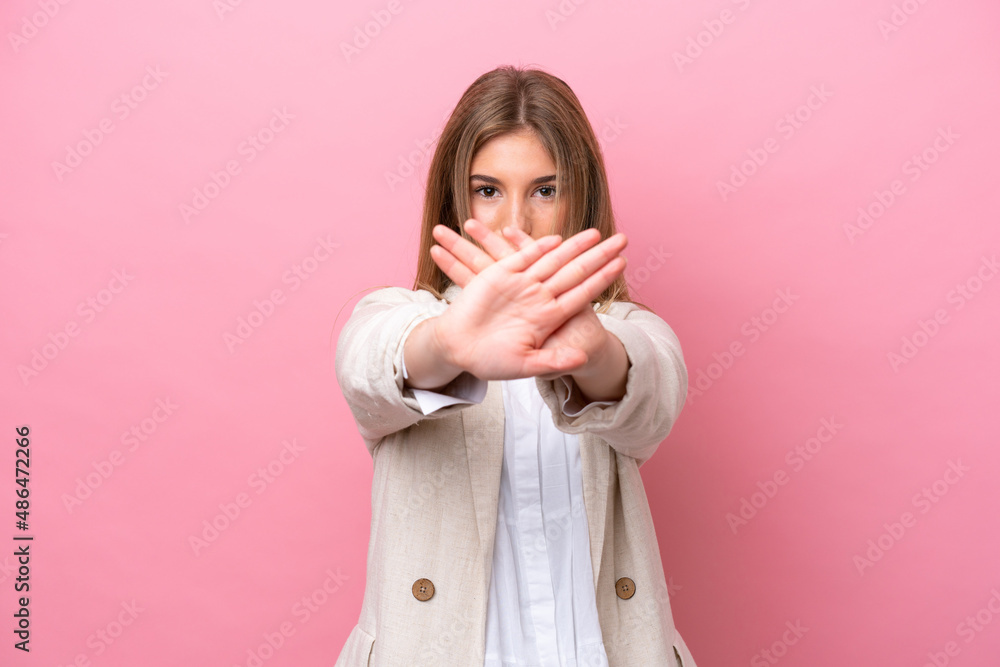 Young caucasian woman isolated on pink bakcground making stop gesture with her hand to stop an act Young caucasian woman isolated on pink bakcground making stop gesture with her hand to stop an act