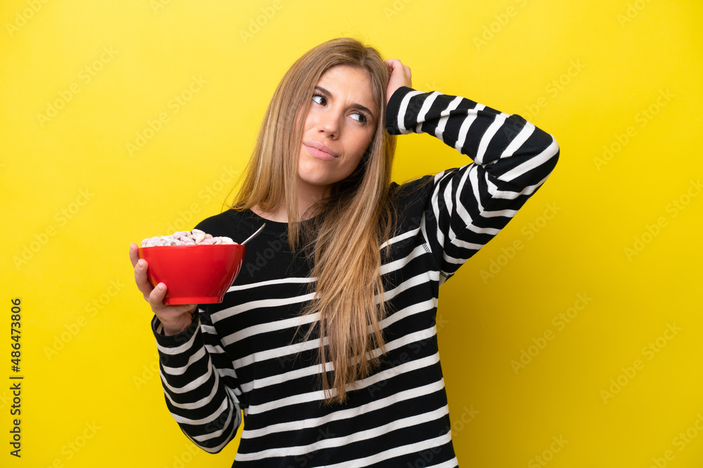 Young caucasian woman holding a bowl of cereals isolated on yellow background having doubts and with confuse face expression Young caucasian woman holding a bowl of cereals isolated on yellow background having doubts and with confuse face expression