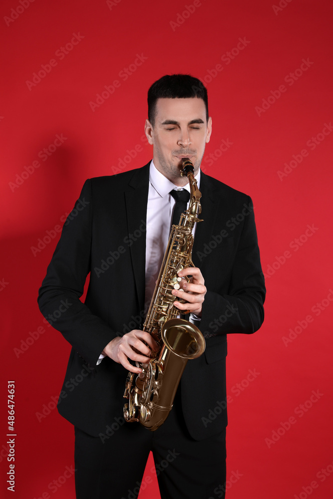 Naklejka premium Young man in elegant suit playing saxophone on red background