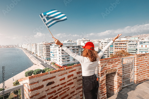 Happy traveller girl with flag on the top viewpoint of a White Tower in Thessaloniki. The concept of citizenship or learning Greek language in university