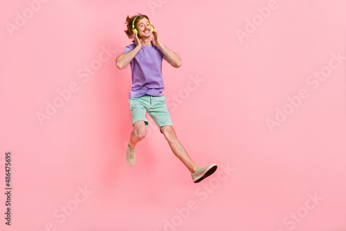 Full length body size view of attractive cheerful guy jumping listening hit song isolated over pink pastel color background