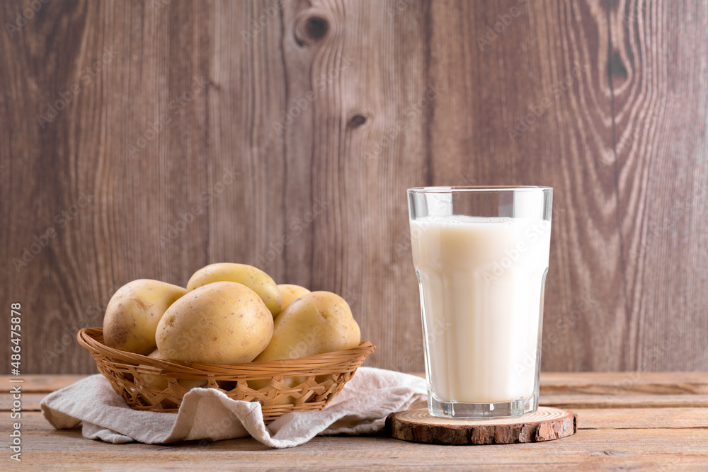 Vegan potato milk in a glass and potato tubers on brown wooden background. Close up. Plant based alternative milk replacer and lactose free, Trendy healthy vegetarian and vegan drink concept Vegan potato milk in a glass and potato tubers on brown wooden background. Close up. Plant based alternative milk replacer and lactose free, Trendy healthy vegetarian and vegan drink concept