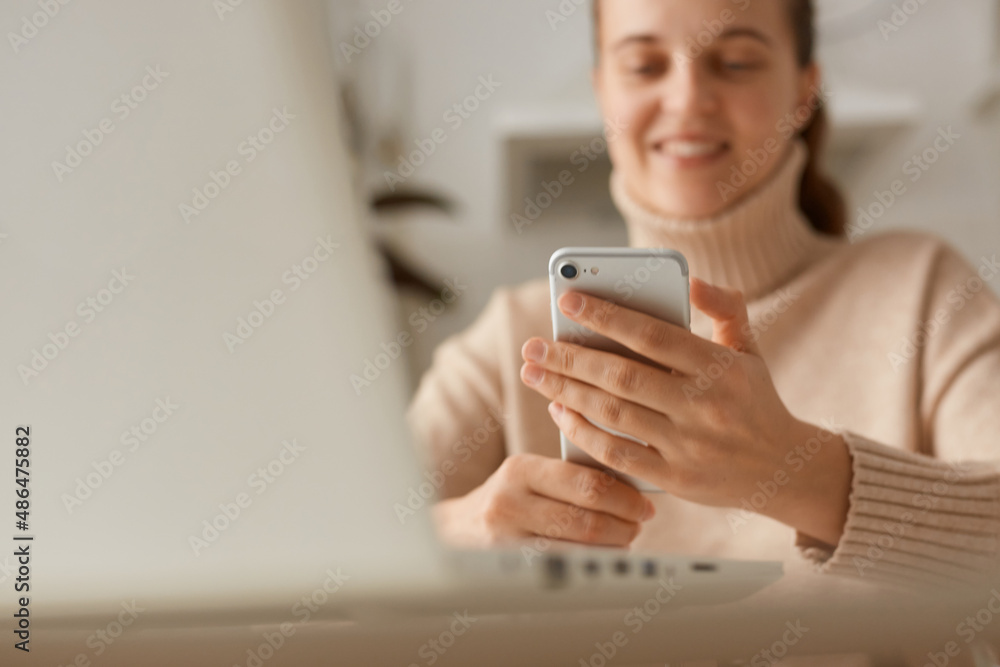 Closeup portrait of woman wearing beige sweater holding smart phone in hands, using cell phone for checking social networks, communicating online with friends.