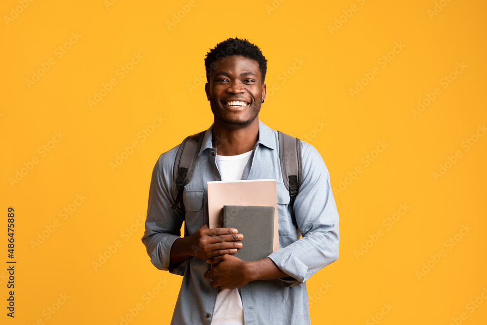 Positive african american guy student with books on yellow Positive african american guy student with books on yellow