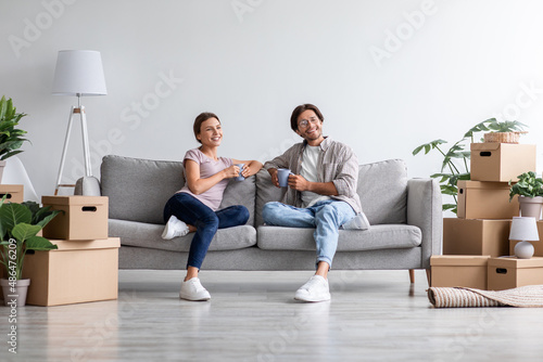 Smiling dreaming european millennial family relaxing on sofa in living room interior with cardboard boxes