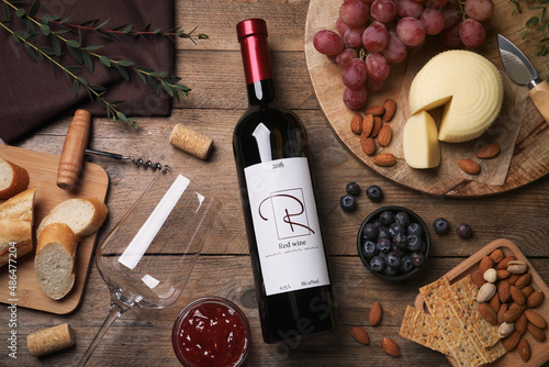 Bottle of red wine with glass and appetizers on wooden table, flat lay