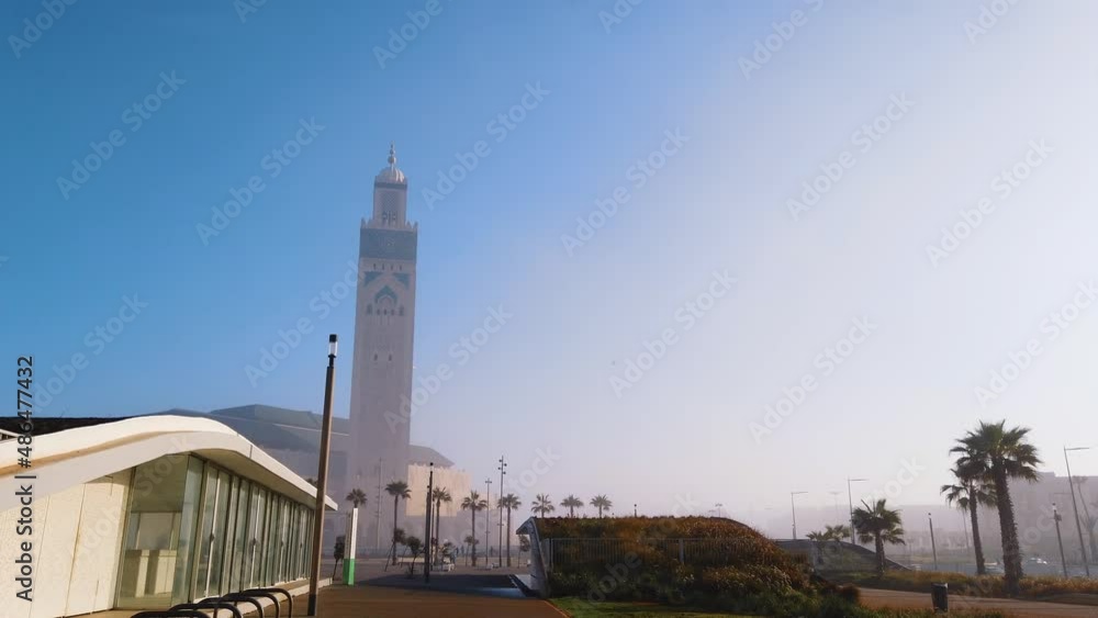 stabilized traveling shot of Hassan II mosque from walk alley - view with people and palm trees in a sunny day - Casablanca, Morocco stabilized traveling shot of Hassan II mosque from walk alley - view with people and palm trees in a sunny day - Casablanca, Morocco