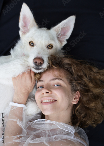 Valokuva portrait of a cute girl - a teenager of 17-18 years old next to her white dog on a dark background
