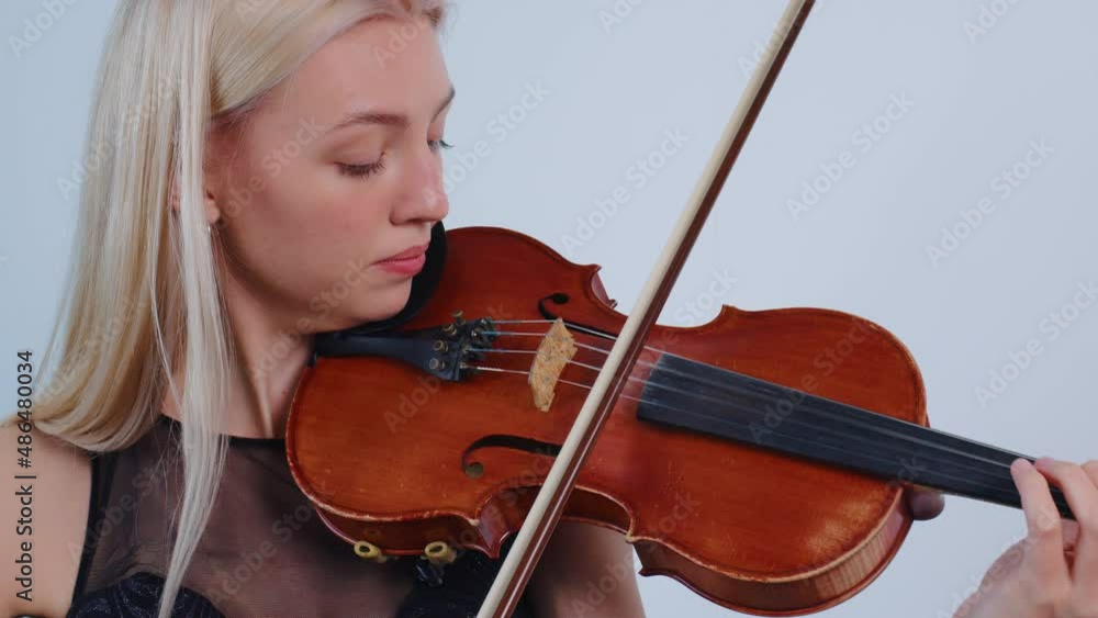 Beautiful violinist playing violin with inspiration indoor. Blonde young woman is learning melody. Female european fiddler rehearsing before exam, concert, performance. Hobby, music, fiddle. Close up Beautiful violinist playing violin with inspiration indoor. Blonde young woman is learning melody. Female european fiddler rehearsing before exam, concert, performance. Hobby, music, fiddle. Close up