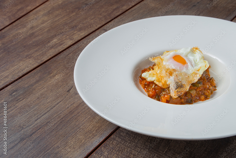 Still life of ratatouille with fried egg on a white plate on a wooden board. Concept of traditional Spanish gastronomy. Still life of ratatouille with fried egg on a white plate on a wooden board. Concept of traditional Spanish gastronomy.