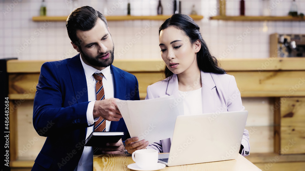 bearded businessman and asian businesswoman working remotely in cafe bearded businessman and asian businesswoman working remotely in cafe